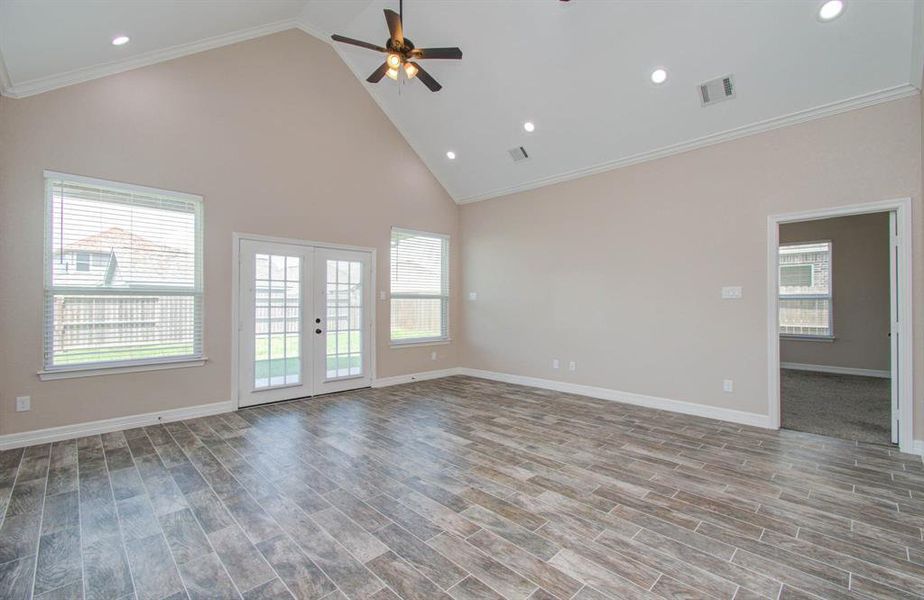 This is a spacious, well-lit living area featuring high ceilings with recessed lighting, large windows, French doors leading outside, and stylish tile flooring that emulates a wood finish.