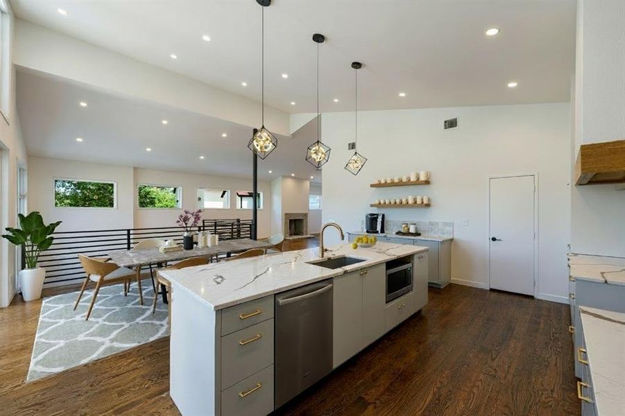 Kitchen featuring hanging light fixtures, recessed lighting, stainless steel appliances, a kitchen island with sink, and light stone counters