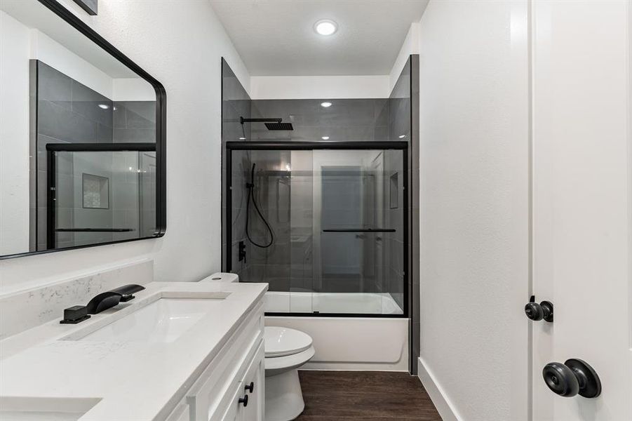 Full bathroom with vanity, hardwood / wood-style flooring, bath / shower combo with glass door, and toilet