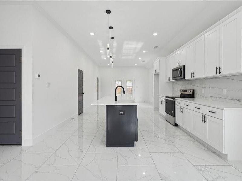 Kitchen with light tile patterned floors, appliances with stainless steel finishes, a kitchen island with sink, decorative backsplash, and white cabinets