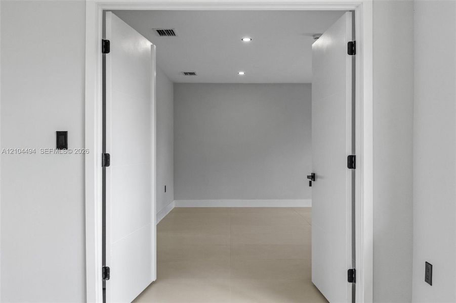 Double interior doors featuring matte black hardware, recessed ceiling lighting, and neutral large-format tile flooring