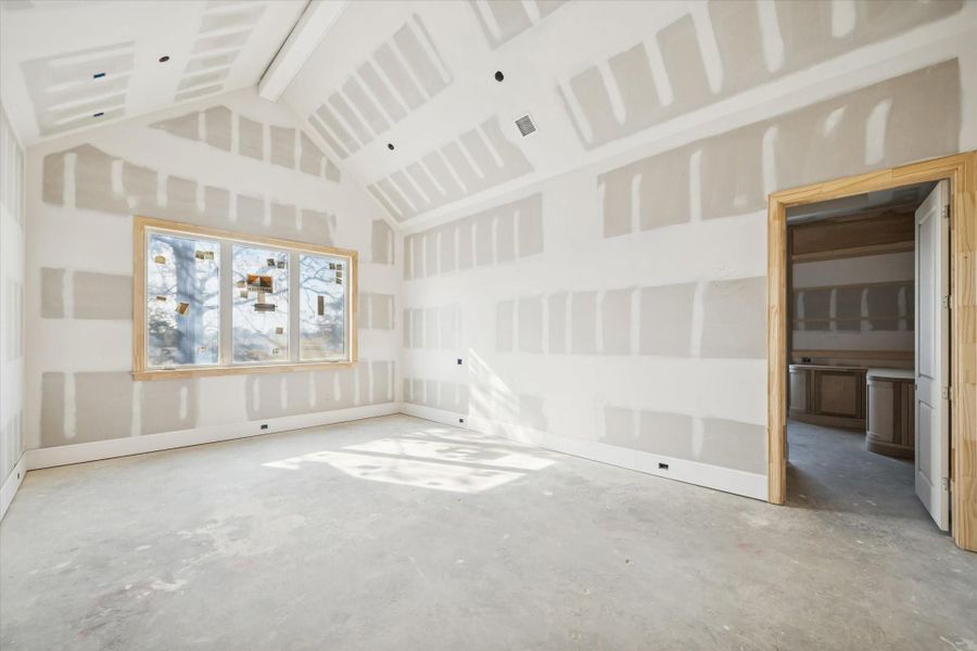 The primary bedroom offers impressive scale with its vaulted ceiling and a full wall of windows overlooking the backyard. The framing highlights the future feature beam and trim details that will give the room its warm character. A calm, private retreat thoughtfully positioned on the first floor.