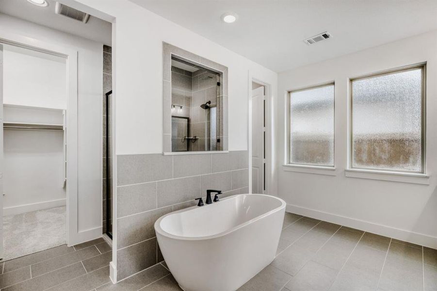 Full bathroom featuring tile walls, a shower stall, light tile patterned floors, a freestanding bath, and a walk in closet