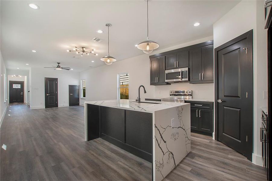 Kitchen with appliances with stainless steel finishes, hardwood / wood-style flooring, light stone counters, ceiling fan, and pendant lighting