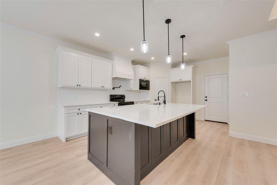 Kitchen featuring white cabinetry, light hardwood / wood-style floors, black appliances, and an island with sink