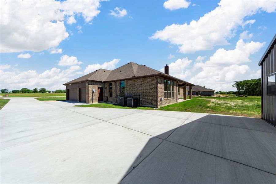 Back of house with brick siding, a garage, a chimney, driveway, and central AC unit Back of house with brick siding, a garage, a chimney, driveway, and central AC unit