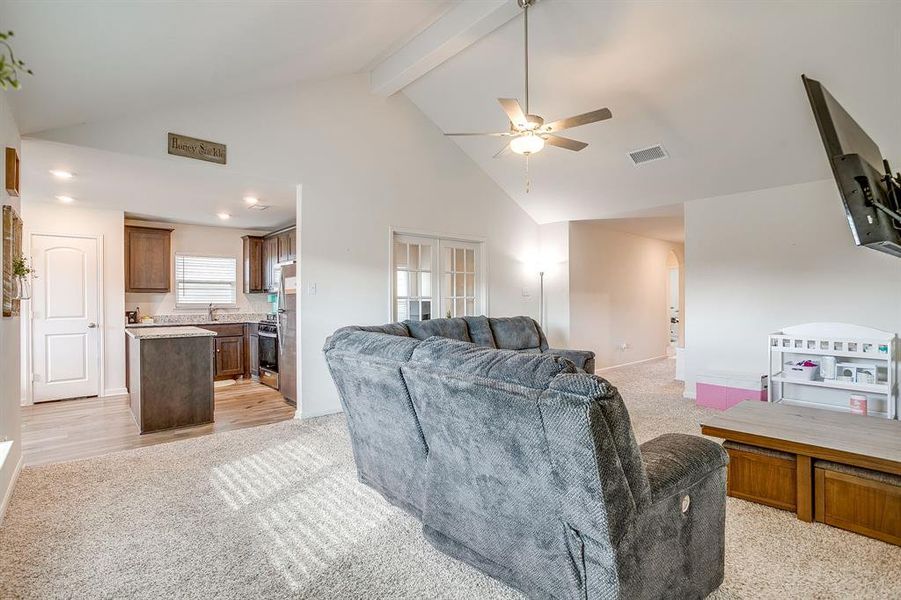 Living area featuring high vaulted ceiling, light carpet, a ceiling fan, and beamed ceiling