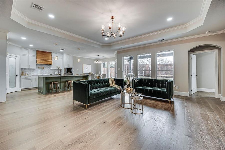 Living room featuring a raised ceiling, crown molding, a notable chandelier, and light wood-type flooring