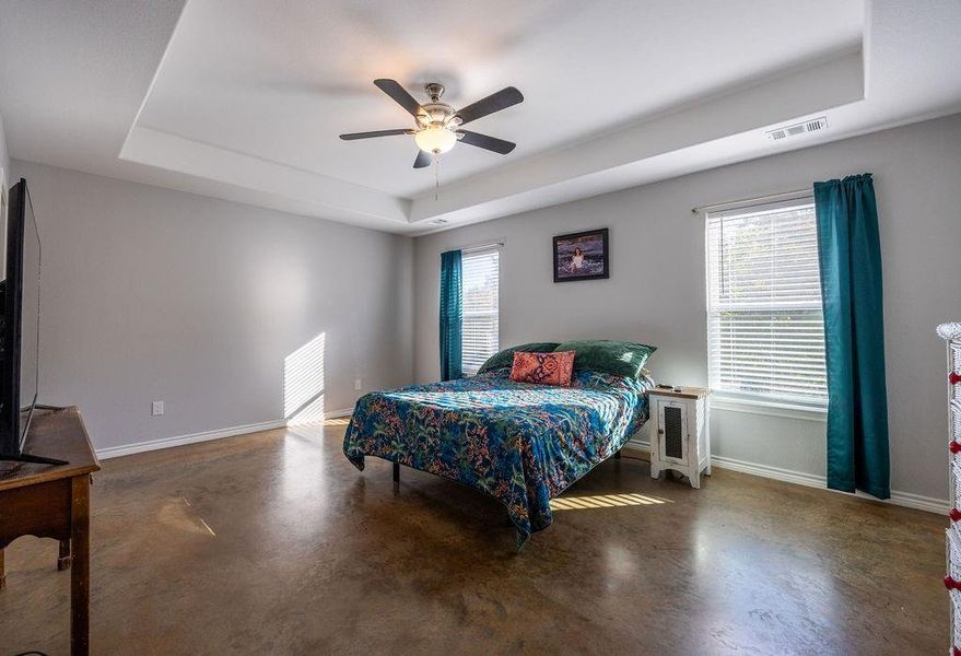 Bedroom with a raised ceiling, multiple windows, and concrete flooring