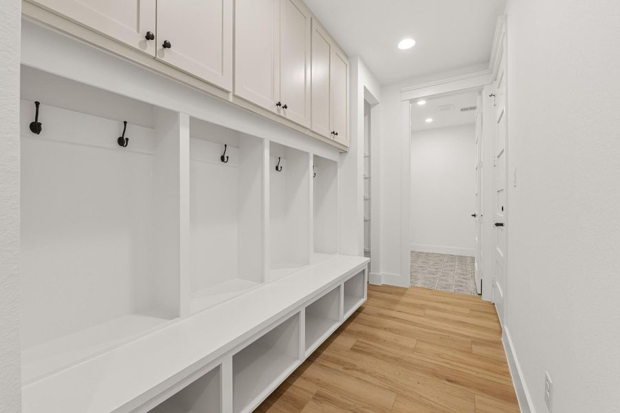 This photo showcases a stylish mudroom with built-in storage cubbies, coat hooks, and overhead cabinets. The space features a bright, clean design with tile flooring and recessed lighting, offering both thoughtful functionality right off of the garage and the laundry room. This photo showcases a stylish mudroom with built-in storage cubbies, coat hooks, and overhead cabinets. The space features a bright, clean design with tile flooring and recessed lighting, offering both thoughtful functionality right off of the garage and the laundry room.