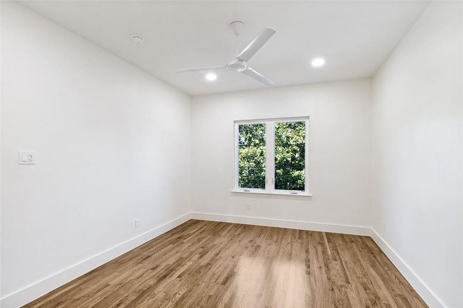 Bright room with wood-finish flooring, white walls, a multi-pane window, modern ceiling fan, and recessed lighting Bright room with wood-finish flooring, white walls, a multi-pane window, modern ceiling fan, and recessed lighting