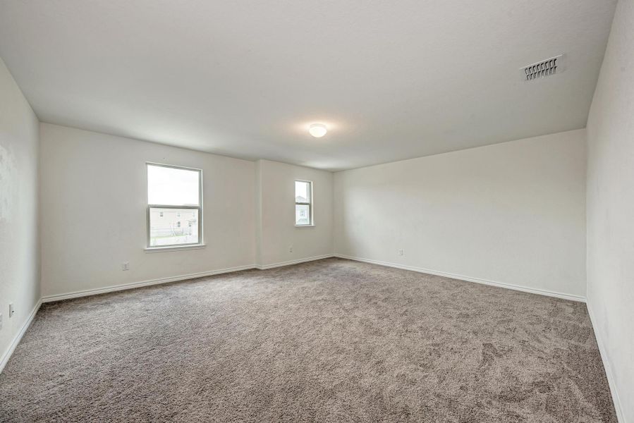 An airy, well-lit bedroom features ample floor space and warm carpeting, ready for personalization.