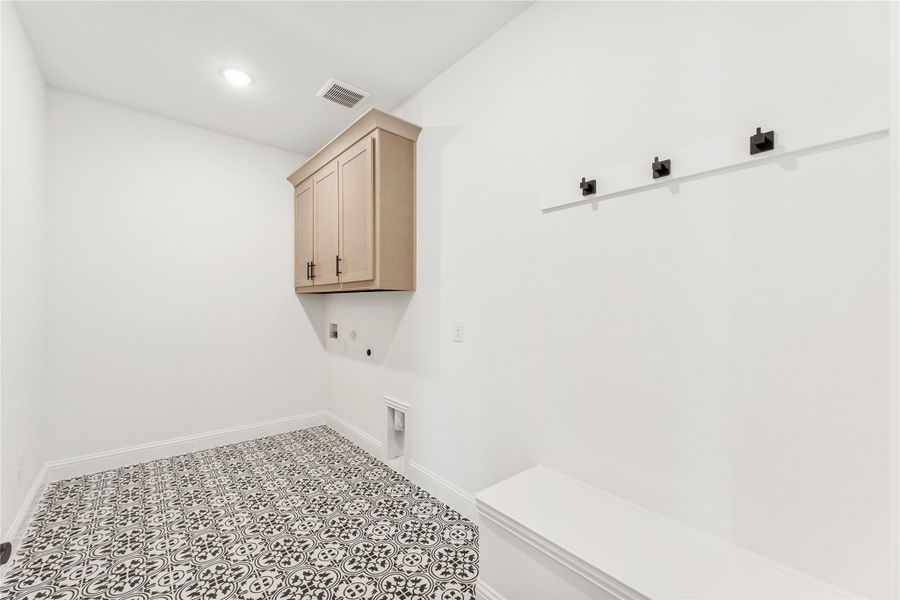 Laundry and mudroom area with patterned tile floor, upper cabinet, wall hooks, and built-in bench