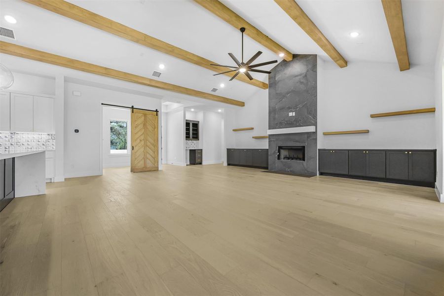 Unfurnished living room featuring a barn door, ceiling fan, recessed lighting, light wood-style flooring, and a fireplace