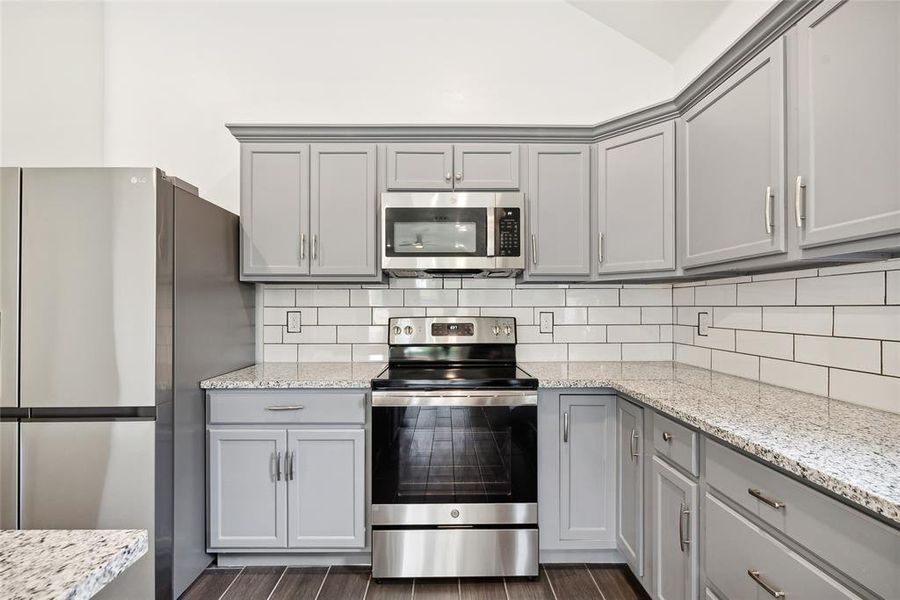 Kitchen featuring dark wood-type flooring, tasteful backsplash, stainless steel appliances, and gray cabinetry