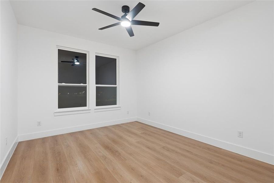 Bright room featuring two large windows, wood-finish flooring, white baseboards, and a modern ceiling fan with integrated lighting Bright room featuring two large windows, wood-finish flooring, white baseboards, and a modern ceiling fan with integrated lighting