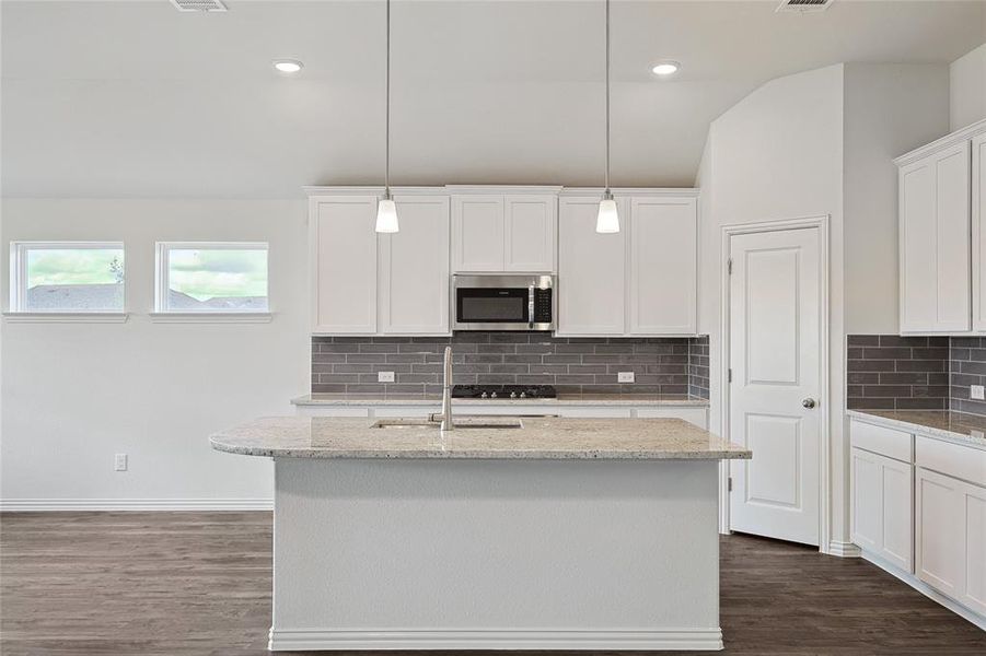 Kitchen featuring backsplash, dark hardwood / wood-style flooring, an island with sink, and decorative light fixtures