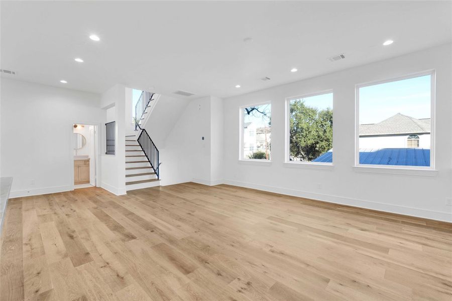 Second-floor main living and kitchen area with abundant natural light, high ceilings, engineered wood floors, custom built-ins, and a stunning custom fireplace as the focal point. Features an oversized island with Taj Mahal quartzite countertops and integrated appliances.