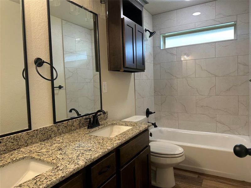 Bathroom featuring double vanity, wood finished floors, and washtub / shower combination Bathroom featuring double vanity, wood finished floors, and washtub / shower combination