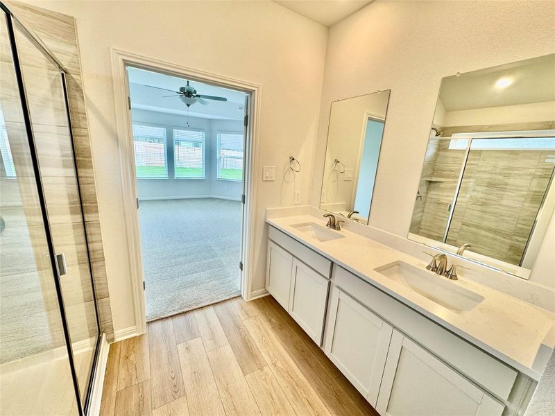 Full bathroom with a stall shower, double vanity, light wood-style flooring, and ceiling fan