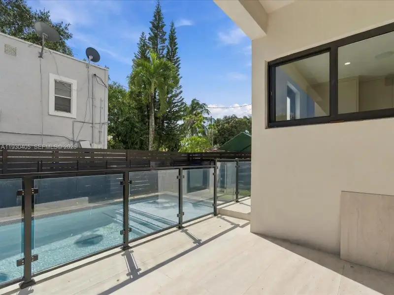 Covered patio with large-format tile flooring, swimming pool, glass railing system, and horizontal wood-slat privacy fencing Covered patio with large-format tile flooring, swimming pool, glass railing system, and horizontal wood-slat privacy fencing
