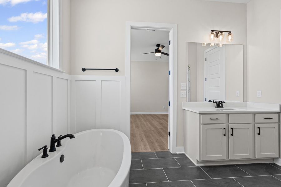 Full bath with vanity, a soaking tub, dark tile patterned floors, ceiling fan, and a decorative wall Full bath with vanity, a soaking tub, dark tile patterned floors, ceiling fan, and a decorative wall