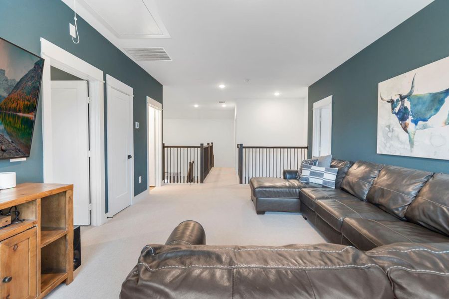 This photo showcases a cozy upstairs living area with a large leather sectional sofa, modern decor, and a flat-screen TV. The room features a calming blue accent wall, soft carpet, and ample natural light, making it an inviting space for relaxation. This photo showcases a cozy upstairs living area with a large leather sectional sofa, modern decor, and a flat-screen TV. The room features a calming blue accent wall, soft carpet, and ample natural light, making it an inviting space for relaxation.