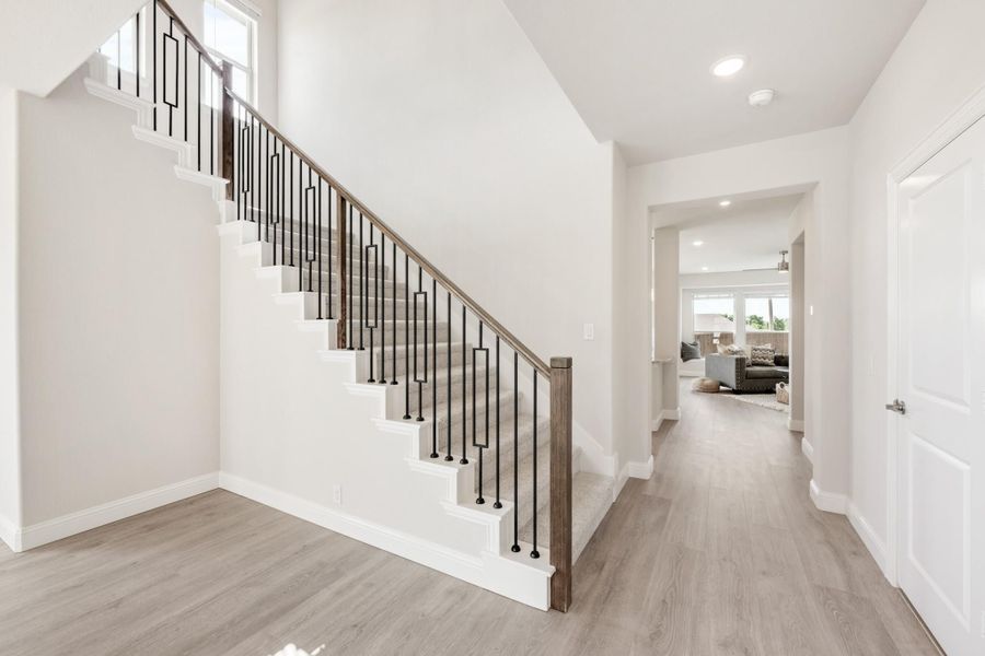 Entryway with staircase featuring black metal balusters, wood handrail, and light gray hardwood floors leading to living room
