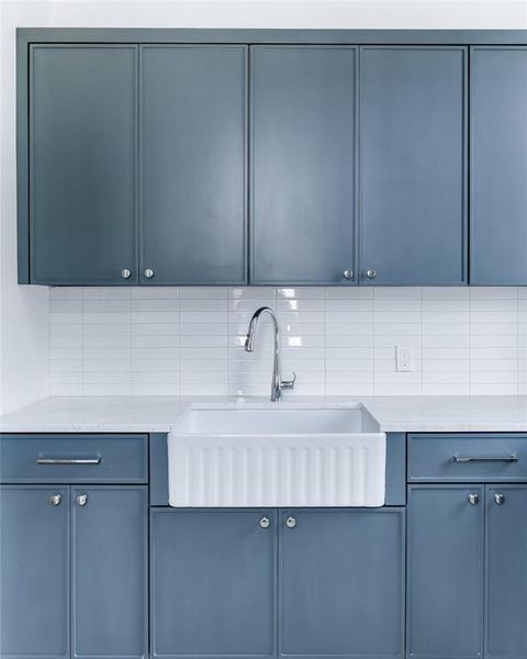 Kitchen with blue cabinetry, tasteful backsplash, sink, and light stone countertops