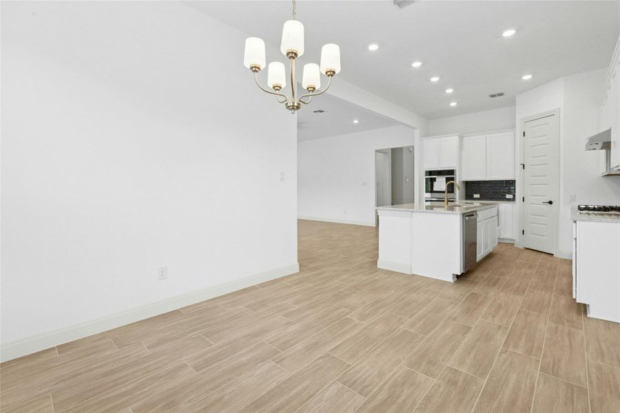 Kitchen featuring a chandelier, open floor plan, tasteful backsplash, decorative light fixtures, and light stone counters Kitchen featuring a chandelier, open floor plan, tasteful backsplash, decorative light fixtures, and light stone counters