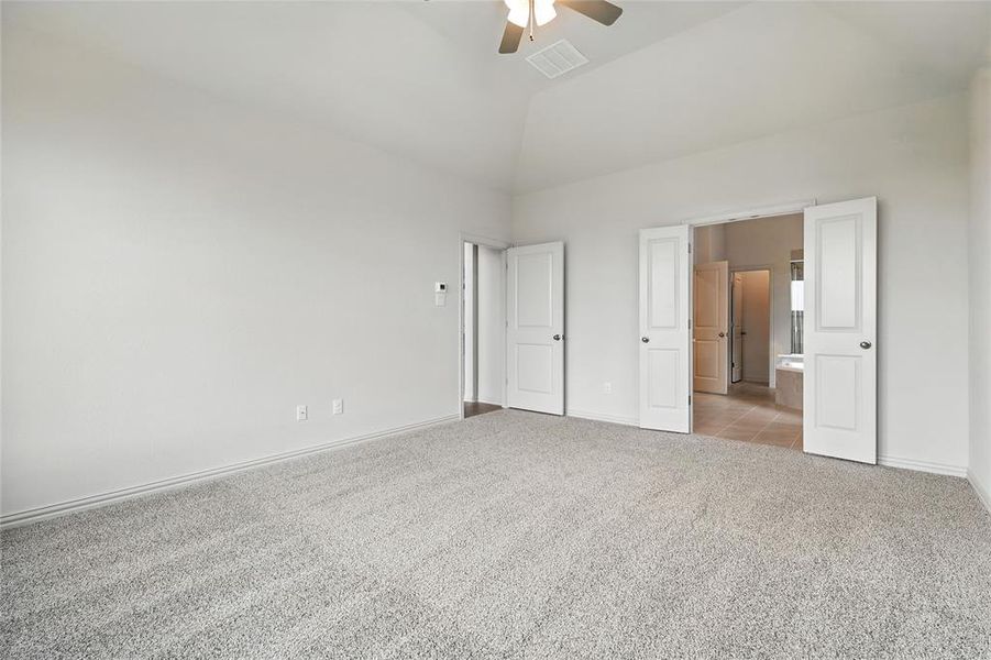 Unfurnished bedroom with carpet flooring, vaulted ceiling, ceiling fan, and ensuite bath