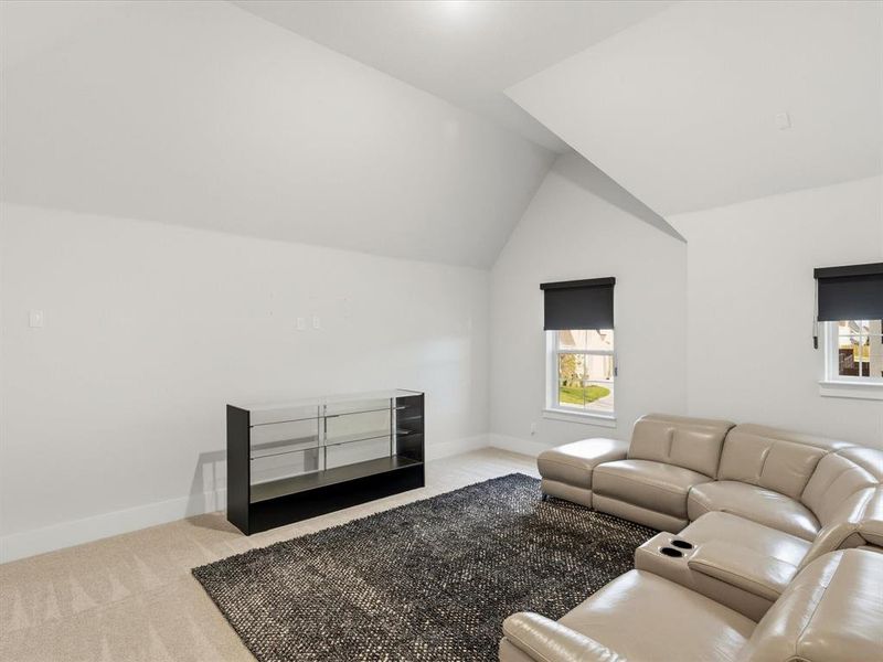 Spacious bonus room featuring vaulted ceilings, two windows with roller shades, and light neutral carpeting Spacious bonus room featuring vaulted ceilings, two windows with roller shades, and light neutral carpeting
