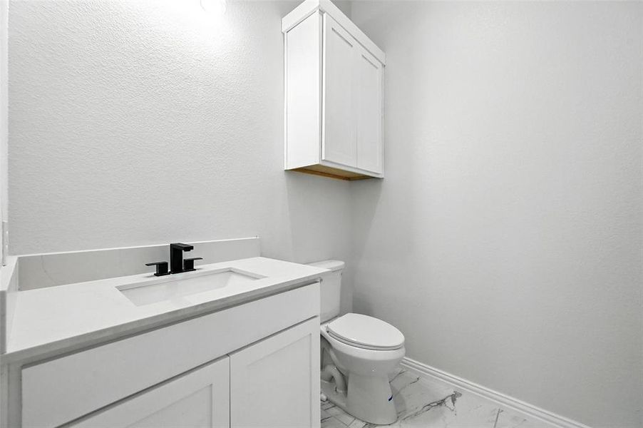 Half bath with vanity, light marble finish flooring, and a textured wall
