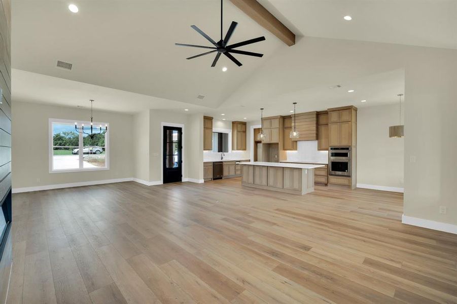 Unfurnished living room featuring beamed ceiling, high vaulted ceiling, ceiling fan with notable chandelier, and light hardwood / wood-style floors