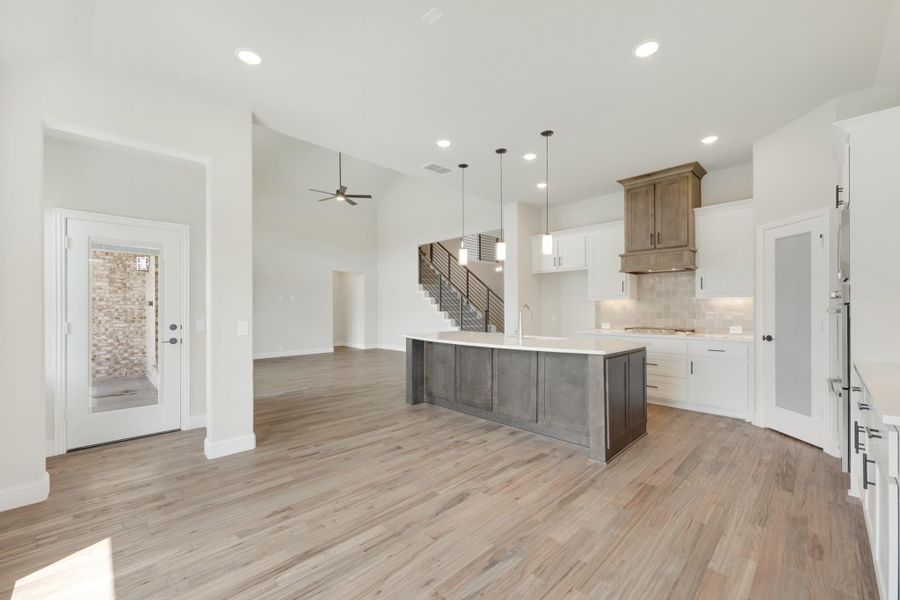 Open kitchen and living area with large island, white cabinets, wood floors, and high ceilings Open kitchen and living area with large island, white cabinets, wood floors, and high ceilings