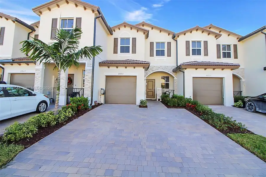 Mediterranean-style exterior featuring stucco siding, stone veneer accents, paver driveway, attached multi-car garages, and recessed entryways Mediterranean-style exterior featuring stucco siding, stone veneer accents, paver driveway, attached multi-car garages, and recessed entryways
