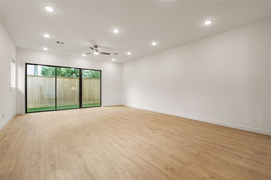 Sunlit living retreat — floor-to-ceiling multi-slide glass doors opening directly to the private yard, framed by warm wood flooring and recessed LED lighting.