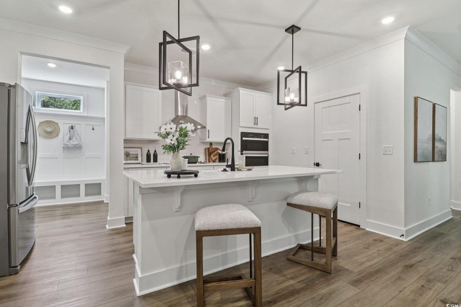 Kitchen featuring appliances with stainless steel finishes, white cabinetry, decorative light fixtures, wall chimney range hood, and crown molding