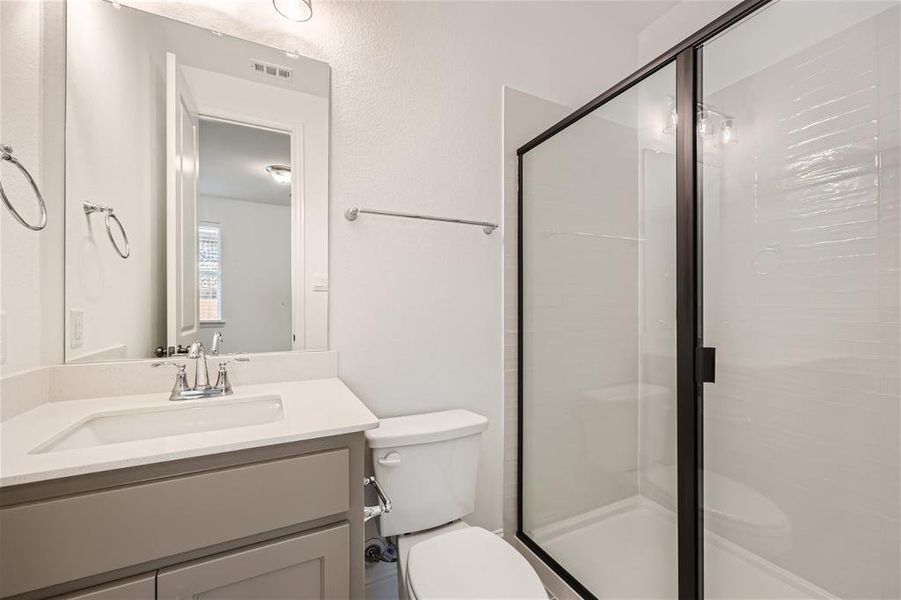 Bathroom with vanity with extensive cabinet space, an enclosed shower, and toilet