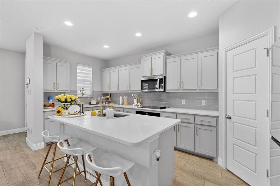 The property features a kitchen with light-colored cabinetry, a large central island with seating, stainless steel appliances, and wood-look tile flooring