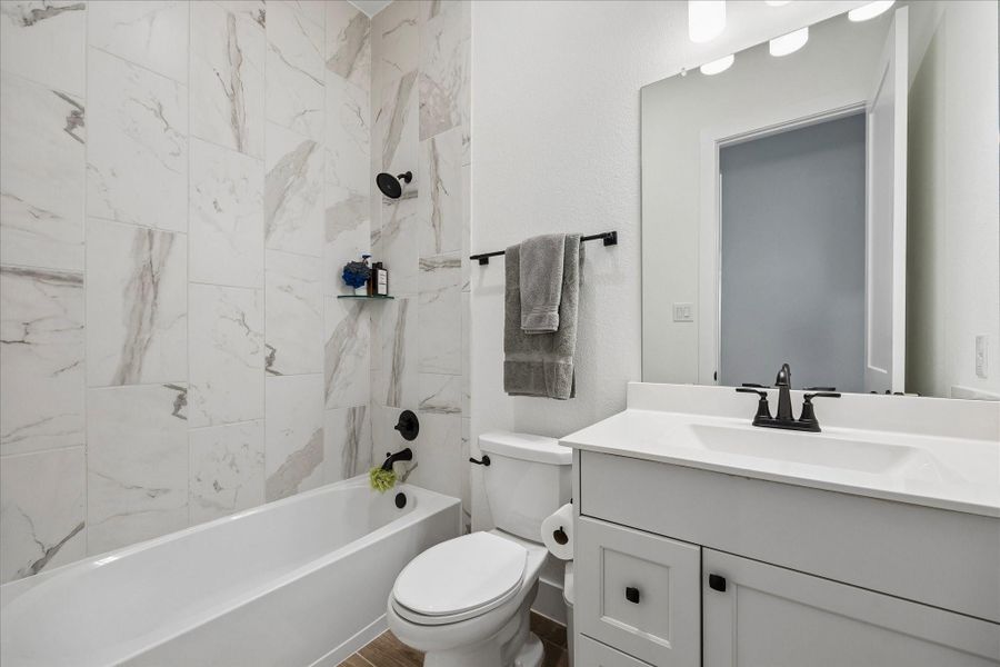 Another secondary bath featuring a full height tile surround with clean, modern veining and matte black fixtures for contrast. Crisp white vanity with quartz countertop and streamlined lighting keeps the space bright and cohesive. Another secondary bath featuring a full height tile surround with clean, modern veining and matte black fixtures for contrast. Crisp white vanity with quartz countertop and streamlined lighting keeps the space bright and cohesive.