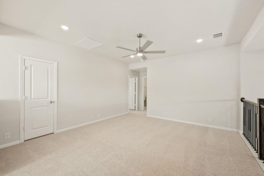 Empty bedroom with beige carpet, ceiling fan, and open doorway to ensuite bathroom