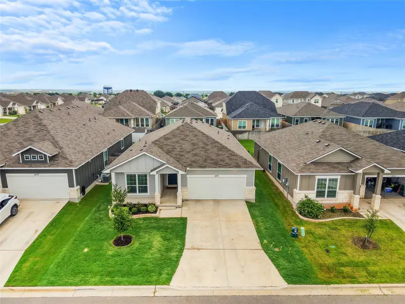 An aerial view captures the uniform design of multiple single-story homes, each with a neat lawn and concrete driveway. An aerial view captures the uniform design of multiple single-story homes, each with a neat lawn and concrete driveway.