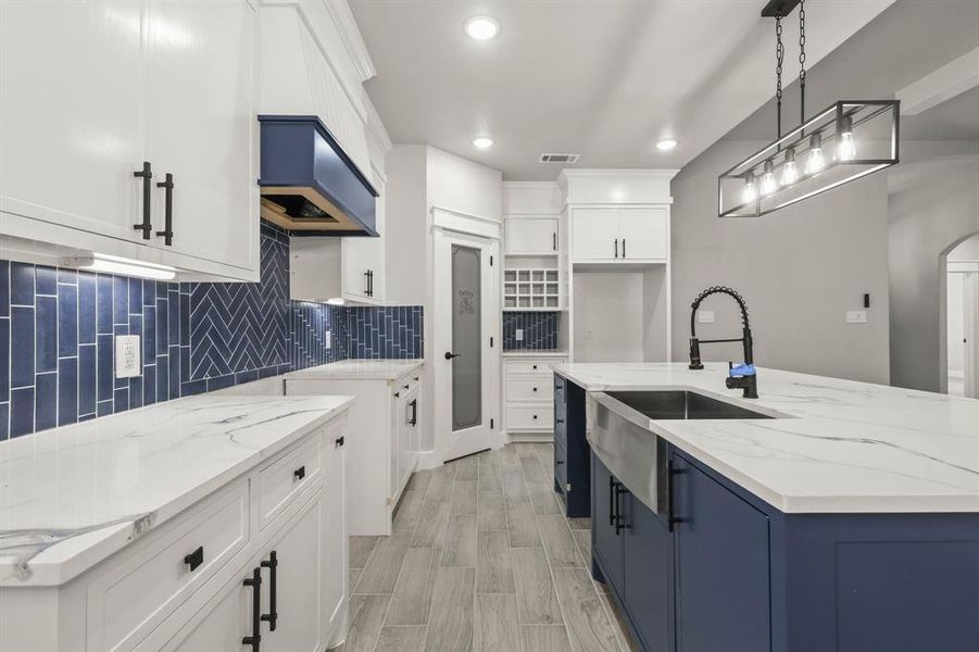 Kitchen with a sink, light stone countertops, tasteful backsplash, a kitchen island with sink, and pendant lighting