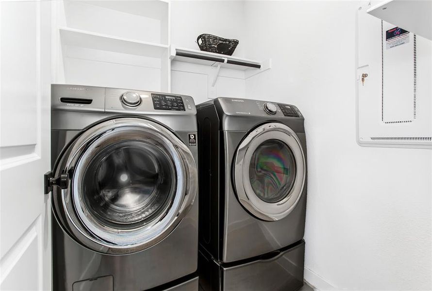Laundry area featuring a washer and dryer, white shelving, and a wall-mounted utility panel