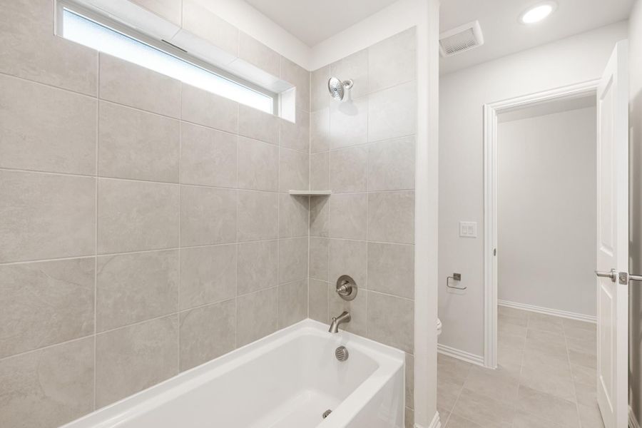 Bathroom with white soaking tub, gray tile surround, built-in shelf niche, and overhead shower fixture