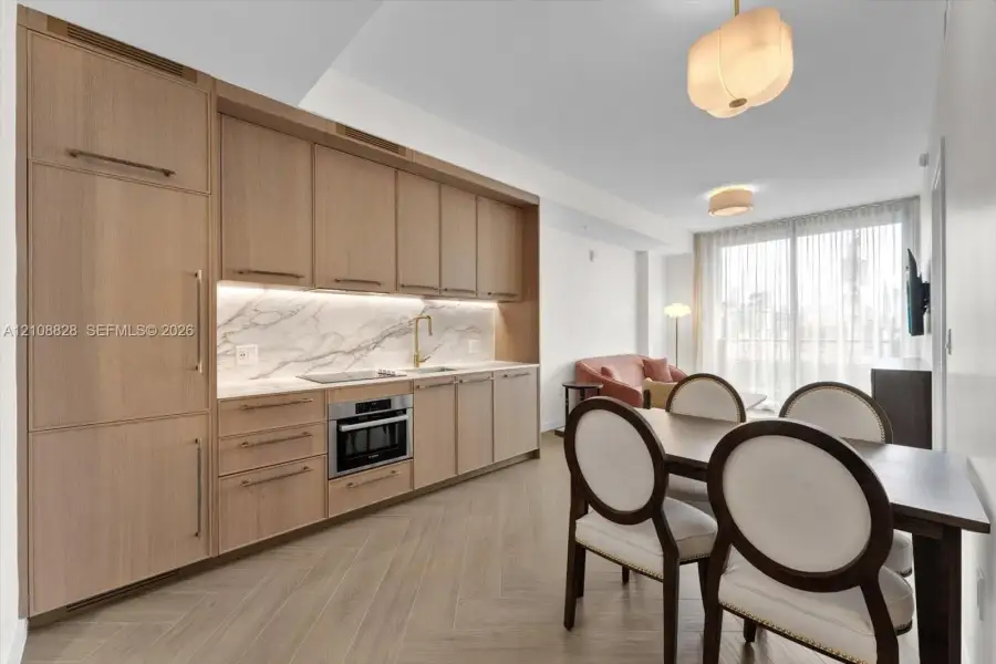 Kitchen featuring flat-panel wood cabinetry, integrated appliances, stone backsplash, gold-tone hardware, and herringbone wood-finish flooring