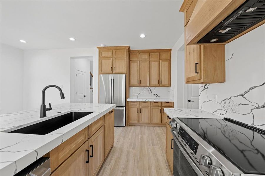 Kitchen with custom exhaust hood, stainless steel appliances, recessed lighting, backsplash, and a sink