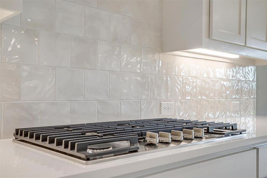 Details with white cabinets, stainless steel gas stovetop, and tasteful backsplash