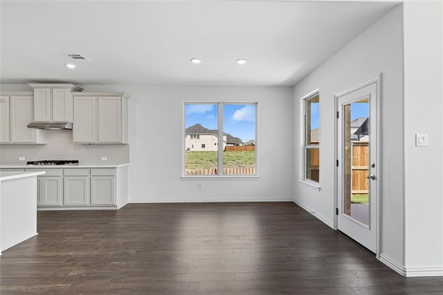 Kitchen with tasteful backsplash, dark wood finished floors, recessed lighting, white cabinetry, and under cabinet range hood Kitchen with tasteful backsplash, dark wood finished floors, recessed lighting, white cabinetry, and under cabinet range hood